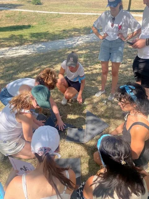 Groupe accroupi qui assemble un grand puzzle géométrique au sol pendant un défi d'équipe MyBestCoaching dans un parc
