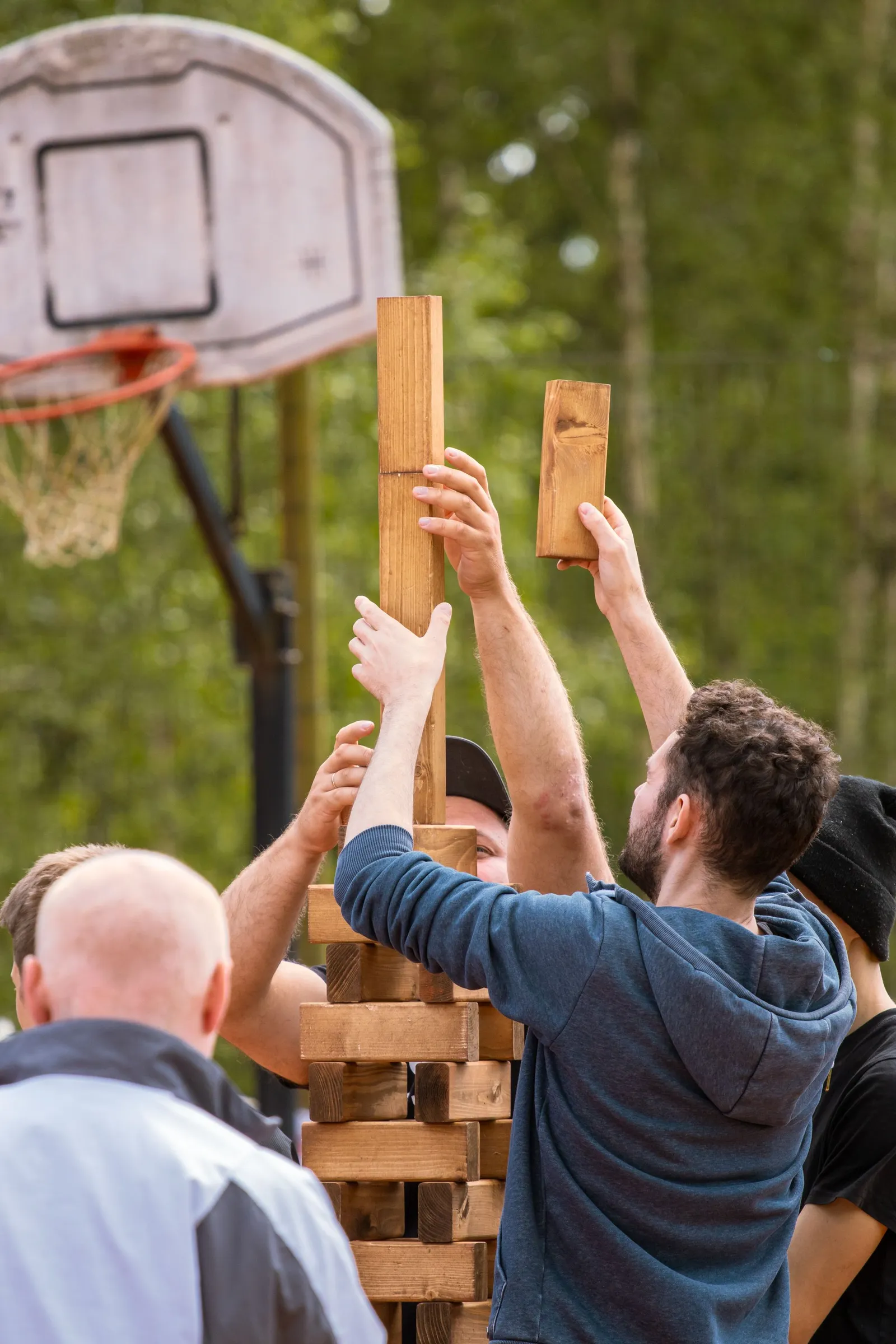 Collègues qui empilent ensemble les blocs d'une tour géante en bois en plein air pendant un défi de cohésion MyBestCoaching