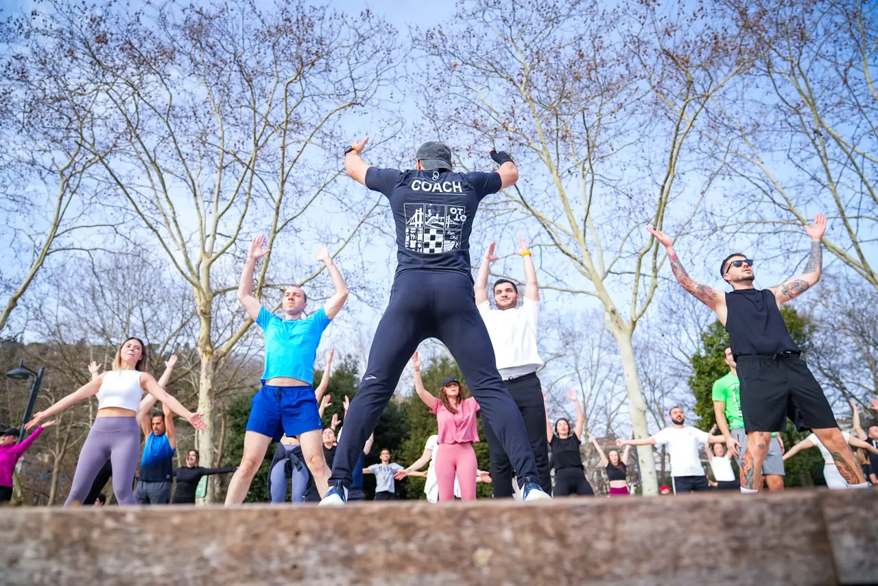 Coach MyBestCoaching menant une séance de bootcamp en plein air, grand groupe de participants enchaînant des jumping jacks dans un parc