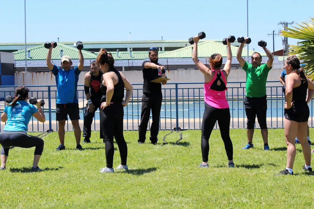 Collaborateurs en cercle lors d'un circuit training collectif en extérieur, haltères en main, encadrés par un coach