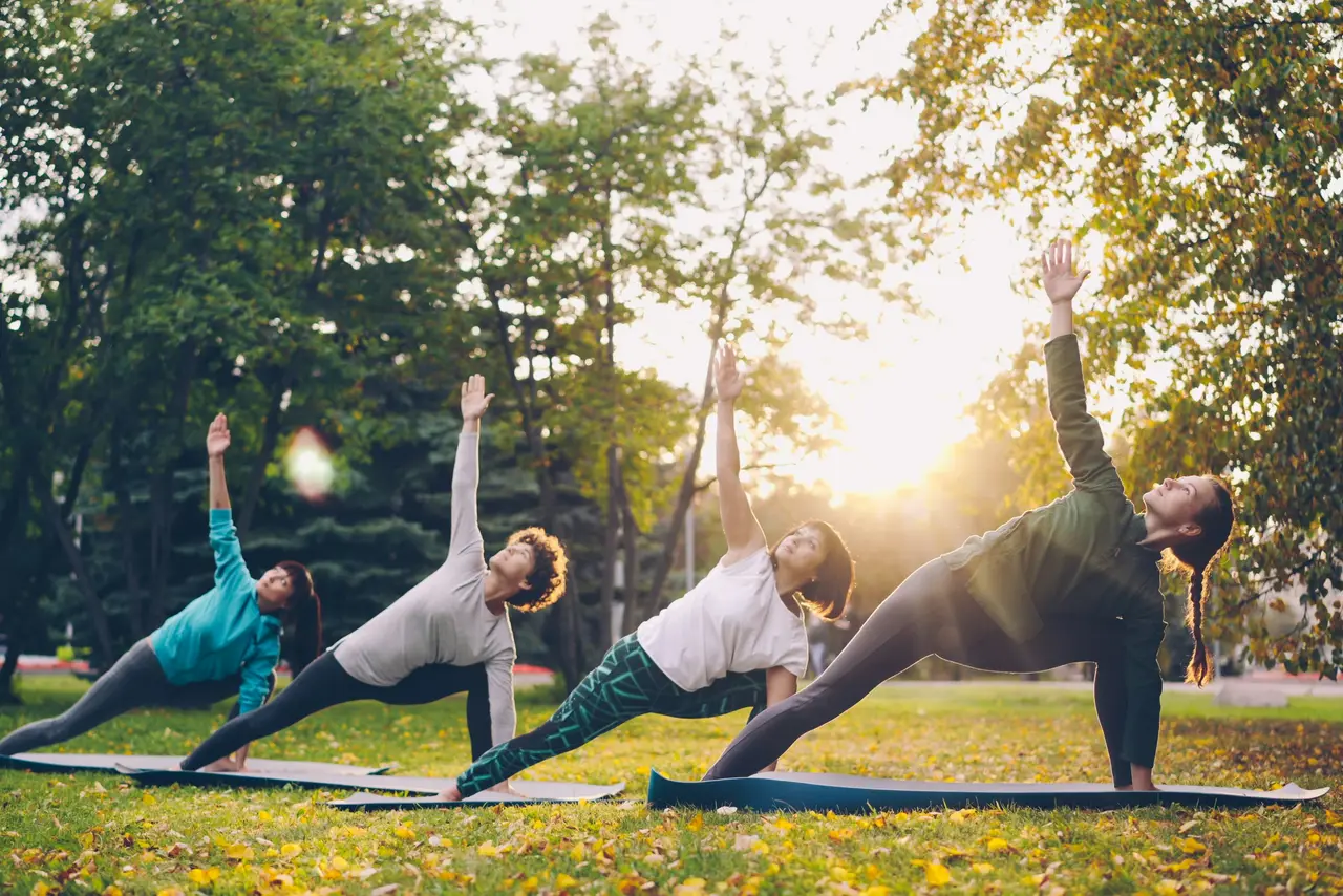 Cours de yoga en groupe en extérieur au coucher du soleil, posture de la planche latérale sur tapis