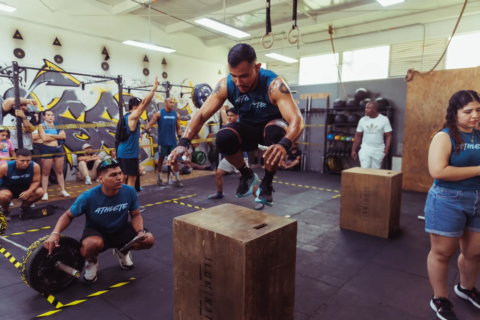 Athlète en plein box jump pendant un WOD collectif, entouré d'autres pratiquants dans une box de CrossFit
